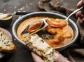 Tomato gazpacho soup with mussels, squid, shrimp in bowl over dark wooden background. Hands holding a spoon with prawn and soup.