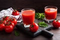 Tomato juice in glass glasses and fresh ripe tomatoes on a branch. Dark wooden background with copy space. Royalty Free Stock Photo