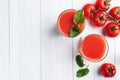 Tomato juice in glass glasses and fresh ripe tomatoes on a branch. White wooden background with copy space. Royalty Free Stock Photo