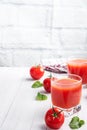 Tomato juice in glass glasses and fresh ripe tomatoes on a branch. White wooden background with copy space. Royalty Free Stock Photo