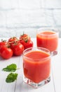 Tomato juice in glass glasses and fresh ripe tomatoes on a branch. White wooden background with copy space. Royalty Free Stock Photo