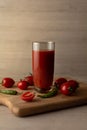 Tomato juice in a tall glass glass, cherry tomatoes, hot peppers on a cutting board, wooden background. Studio shot