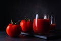 Tomato juice in a transparent glass with fresh tomatoes on a black surface against the background of a soft backdrop close-up. Royalty Free Stock Photo