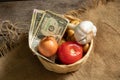 tomato onion garlic potatoes in a wicker basket with dollars on a wooden table, vegetables