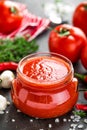 Tomato paste, puree in glass jar and fresh tomatos on dark background. Hot vegetable sauce with chili pepper ant tomatoes