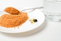 Tomato protein soup powder on a spoon. Meal replacement. Dry soup. Multivitamins, astaxanthin, fish oil, omega pills on a plate.