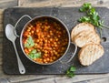 Tomato sauce braised chickpeas in a pot, and grilled bread. Delicious vegetarian lunch on a rustic wooden background