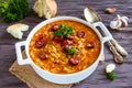 Tomato soup with orzo and smoked sausages in white casserole on wooden rustic table. Fresh bread and parsley, vintage spoon Royalty Free Stock Photo