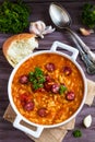 Tomato soup with orzo and smoked sausages in white casserole on wooden rustic table. Fresh bread and parsley, vintage spoon Royalty Free Stock Photo