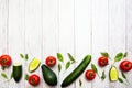 Tomatoes, avocado, cucumbers, whole and halves, spinach leaves and dill, flat lay on a white wooden surface. Healthy food concept. Royalty Free Stock Photo