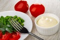 Tomatoes, bowl with mayonnaise, fork on plate with slices of tomato, green peas and parsley on wooden table Royalty Free Stock Photo