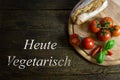 Tomatoes with bread on wooden table, text Heute Vegetarisch