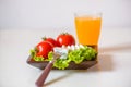 Tomatoes and cheese slices lie on a sheet of fresh salad in a plate. A glass of orange juice stands on the table. Royalty Free Stock Photo