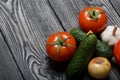 Tomatoes with green ponytails, onion and garlic head. Two green prickly cucumbers with yellow flowers. They lie on the surface of