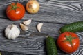 Tomatoes with green ponytails, onion and garlic head. Two green prickly cucumbers with yellow flowers. They lie on the surface of