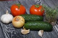 Tomatoes with green ponytails, onion, lemon and garlic head. Two green prickly cucumbers with yellow flowers. A glass with