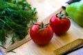 Tomatoes, pepper, herbs and a knife on a wooden board.