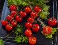 Tomatoes red fist carpal on a black platter with sprigs of green parsley and salad