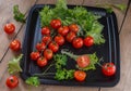 Tomatoes red fist carpal on a black platter with sprigs of green parsley and salad