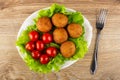 Tomatoes and round fried pies on leaves of lettuce in dish, fork on table. Top view Royalty Free Stock Photo