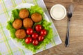 Tomatoes and round fried pies on lettuce in dish on napkin, bowl with mayonnaise and fork on wooden table. Top view Royalty Free Stock Photo