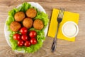 Tomatoes and small fried pies on leaves of lettuce in dish, fork, bowl with mayonnaise on napkin on table. Top view Royalty Free Stock Photo