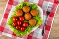 Tomatoes and small fried pies on lettuce in white dish, fork on napkin on wooden table. Top view Royalty Free Stock Photo