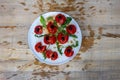 Tomatoes smashed with a fist, decorated with black olives and arugula arranged on a white plate on a wooden table, the pulp