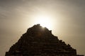 The Tomb of Queen Hetepheres in the Giza pyramid complex with star beams of the rising sun behind it and pigeons flying away