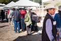 Elegant American gentleman wearing a Stetson hat, viewed from profile, while people are waiting in line to get food