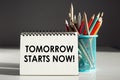 TOMORROW STARTS NOW - inscription on a notebook with colored pencils