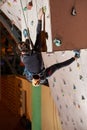 Toned female sportsman putting efforts to reach the top of artificial bouldering wall in indoors gym