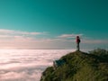 Toned image adult woman with a backpack stands on the edge of a cliff and looking at the sunrise against the blue sky