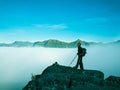 Toned image of an adult woman standing on top of a mountain with a backpack and Alpenstocks against mountains in a fog Royalty Free Stock Photo