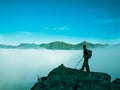 Toned image of an adult woman standing on top of a mountain with a backpack and Alpenstocks against mountains in a fog Royalty Free Stock Photo
