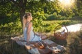 Toned image of beautiful young woman having picnic under big tree looking at evening sun over lake Royalty Free Stock Photo