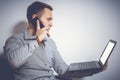 Toned image. Young businessman with laptop and telephone. He looks at the screen and speaks on the mobile Royalty Free Stock Photo