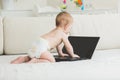 Toned photo of adorable baby boy crawling on bed and touching laptop Royalty Free Stock Photo