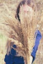 Toned photo of woman hide behind large fluffy bouquet made of dried yellow bushgrass holding in hand.