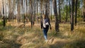 Toned photo of young female hikinh and walking on the field next to big pine tree forest