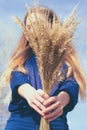 Toned photo of young woman holds dried yellow bushgrass in hands and shows at camera.