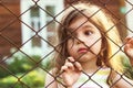 Toned portrait of Sad cute little girl looks through wire fence