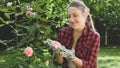 Toned portrait of smiling young woman holding growing pink rose in hand at backyard garden Royalty Free Stock Photo