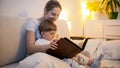 Toned portrait of smiling young woman reading story to her toddler son before going to sleep Royalty Free Stock Photo