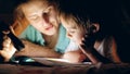 Toned portrait of young mother holding flashlight and reading bedtime story book to her little son lying under blanket Royalty Free Stock Photo