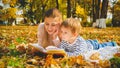 Toned portrait of young mother reading story book to her son lying on autumn leaves at park Royalty Free Stock Photo