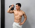 A toned, shirtless Asian man flexes his muscles, the sheen of sweat reflecting his hard work, as he deftly poses with a hefty