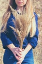 Toned vertical photo of young caucasian woman with long hair is holding dried yellow bushgrass bunch in hands.