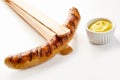 Tongs holding seared sausage beside yellow mustard