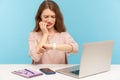 Too late, no time to meet deadline! Upset worried woman employee sitting at workplace and looking at wrist watch Royalty Free Stock Photo